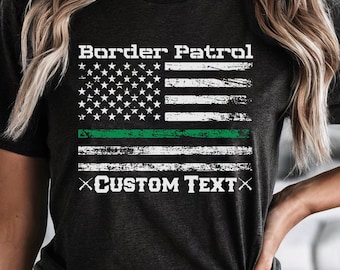 May include: A black t-shirt with a distressed American flag design and the text "Border Patrol" above the flag. A green stripe is added to the flag. The text "CUSTOM TEXT" is below the flag.
