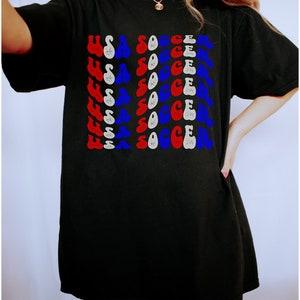 May include: Black t-shirt with a graphic print of "USA SOCCER" repeated in red, white, and blue.