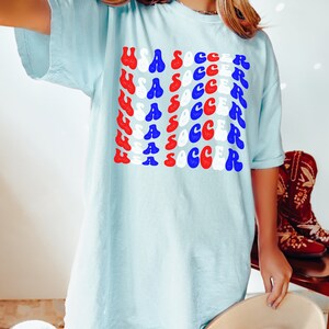 May include: A light blue t-shirt with the words "USA SOCCER" repeated in a retro font in red, white, and blue. The shirt is made of a soft, comfortable material and is perfect for showing your team spirit.