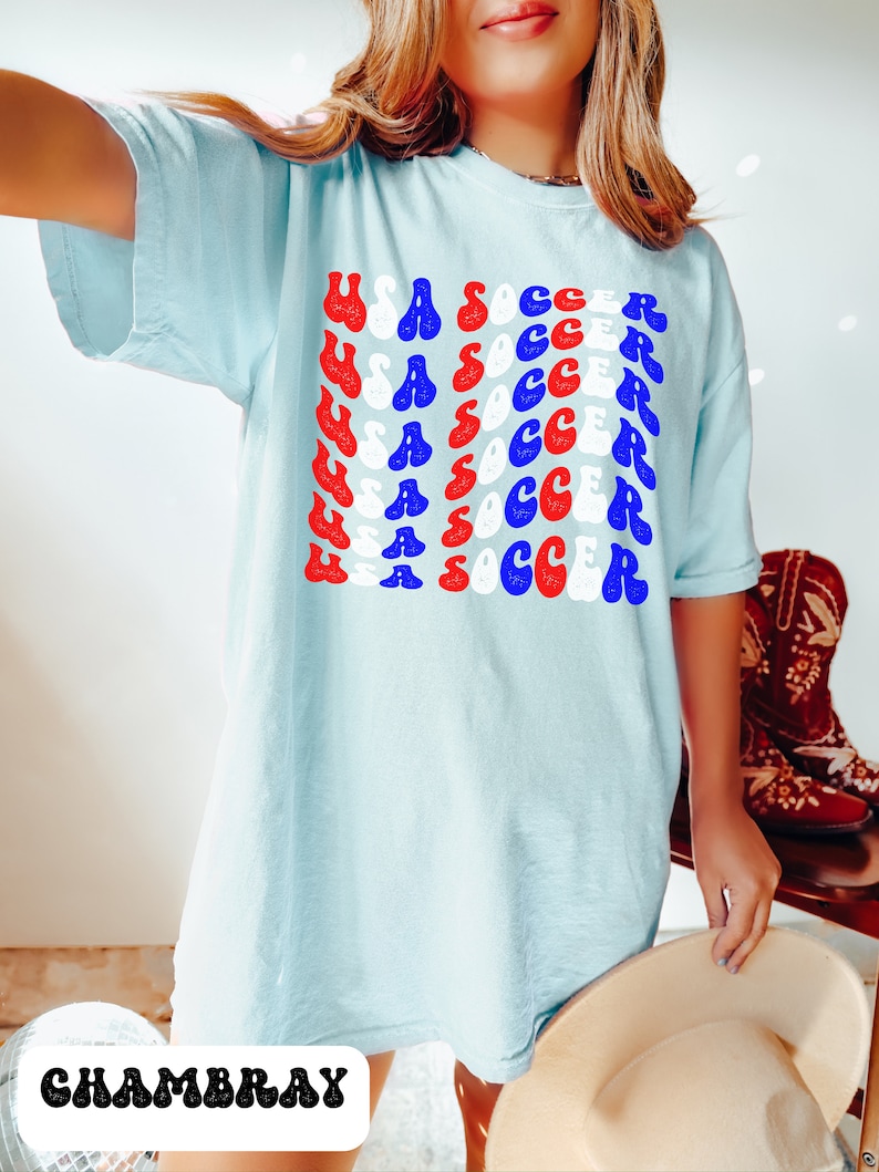 May include: A light blue t-shirt with the words "USA SOCCER" repeated in a retro font in red, white, and blue. The shirt is made of a soft, comfortable material and is perfect for showing your team spirit.