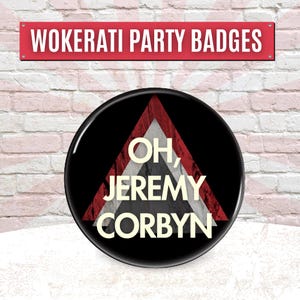 May include: A black badge featuring the text "OH, JEREMY CORBYN" in white, within a red and white triangle. The badge is set against a brick wall, with a red sign above that reads "WOKERATI PARTY BADGES".
