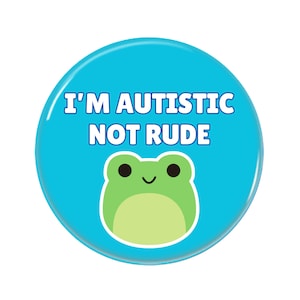 May include: A blue button with the text "I'm autistic not rude" in white letters. A green cartoon frog with black eyes and a smile is below the text.