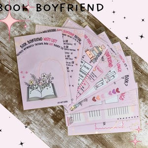 May include: A set of light pink paper sheets featuring printed text and illustrations. The top sheet is titled Book Boyfriend Wish List and displays a line drawing of an open book with flowers growing from the pages, surrounded by stars.