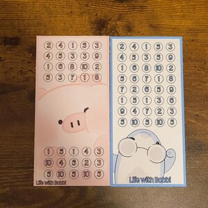 May include: Two colorful cards with number puzzles. One card features a pink pig illustration, the other a blue illustration with glasses. Both cards have the text "Life with Bobbi" at the bottom.