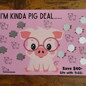 May include: Pink card with the text "I'm kinda pig deal..." and a cartoon pig wearing glasses. The card has 12 silver circles with a pig illustration inside each circle. The text "Save $40+ Life with Bobbi" is at the bottom of the card.