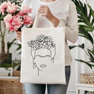 May include: A white tote bag with a black line drawing of a woman's face with flowers in her hair. The woman's face is stylized and has a single eyebrow.