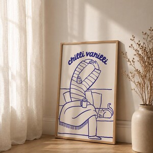 Könnte beinhalten: Ein gerahmter Kunstdruck mit einer blauen Strichzeichnung auf cremefarbenem Hintergrund. Die Illustration zeigt eine Person im gestreiften Oberteil, die sich auf einem Sofa mit einer Katze und einer Tasse streckt, darüber der Text "chilli vanilli".