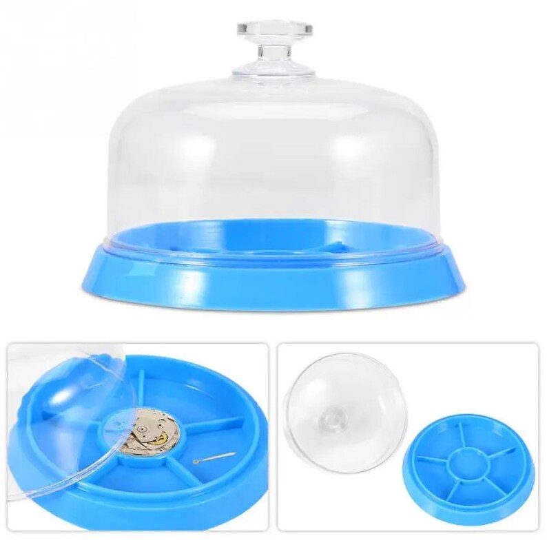 May include: A clear plastic dome with a blue base and a removable tray with compartments. The tray has a small watch movement inside one of the compartments.