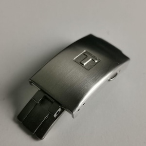 May include: Silver watch band clasp with a brushed finish and a small 'T' logo.