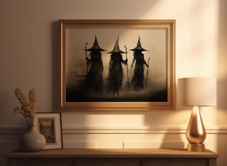 May include: A framed painting of three witches in black robes and pointed hats, walking in a misty forest. The painting is in a gold frame and hangs on a beige wall.