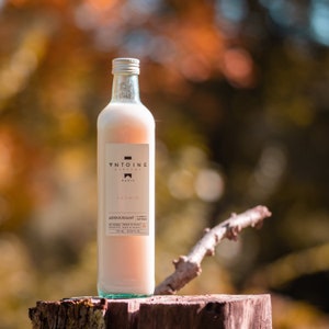 Peut inclure: Une bouteille en verre transparent avec une étiquette blanche sur laquelle est inscrit "V'ntoine Parfums Paris" et "Jasmin Adoucissant Textile". La bouteille est remplie d'un liquide rose clair et repose sur une surface en bois.