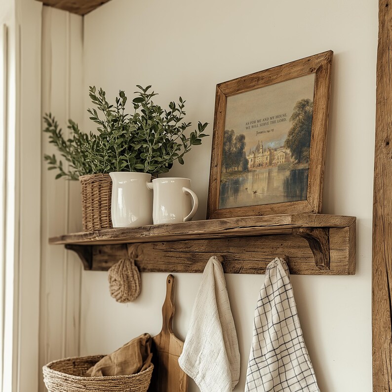 May include: A distressed wooden shelf holds a framed landscape print, white jugs, and a wicker basket with foliage. Below, a woven scrub, wooden chopping board, and hanging tea towels enhance the rustic style.