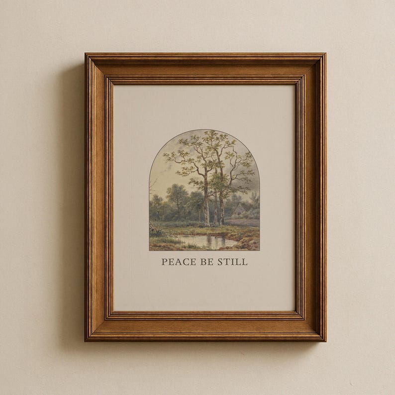 May include: A framed landscape print depicting a tranquil scene with trees, a pond, and a small building. The artwork is set within an arched shape and framed in a brown wooden frame. The text "PEACE BE STILL" is printed below the image.