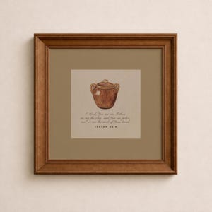May include: A framed print with a watercolour illustration of a brown, lidded pot. The artwork includes text from Isaiah 64:8, set against a beige background, within a brown wooden frame. The overall theme is religious and inspirational.
