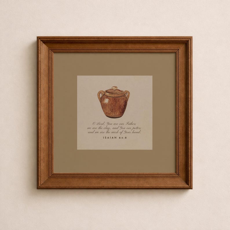 May include: A framed print with a watercolour illustration of a brown, lidded pot. The artwork includes text from Isaiah 64:8, set against a beige background, within a brown wooden frame. The overall theme is religious and inspirational.