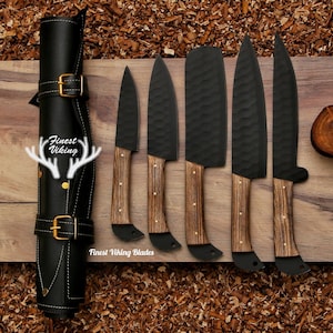 May include: Set of five black kitchen knives with wooden handles, displayed on a wooden surface. The knives are arranged in a row, with the blades facing up. The knives are all different sizes and shapes. The text "Finest Viking Blades" is visible on the surface.
