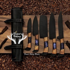 May include: Set of six black kitchen knives with wooden handles and blue resin accents. The knives are arranged on a wooden surface and include a roll-up leather case with the text "Finest Viking" and "Finest Viking Blades".
