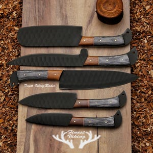 May include: Five black kitchen knives with wooden handles on a wooden surface. The knives have a textured finish and the handles are made of dark wood with a light wood accent. The knives are arranged in a row from largest to smallest. The text "Finest Viking Blades" is visible on the surface.