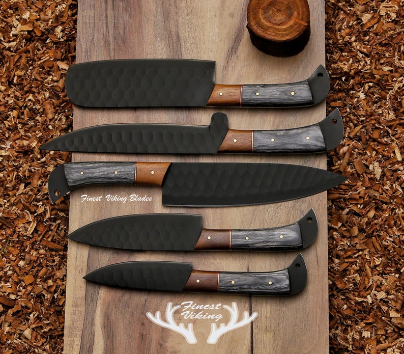 May include: Five black kitchen knives with wooden handles on a wooden surface. The knives have a textured finish and the handles are made of dark wood with a light wood accent. The knives are arranged in a row from largest to smallest. The text "Finest Viking Blades" is visible on the surface.