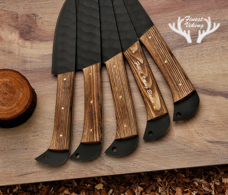 May include: Set of five black knives with wooden handles. The handles are a dark brown wood with a light brown grain. The knives have a hammered finish and are engraved with "Finest Viking Blades".