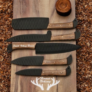 May include: Five black kitchen knives with wooden handles on a wooden surface. The knives have a hammered finish and the handles are made of dark wood with light wood accents. The knives are arranged in a row, with the largest knife at the top and the smallest knife at the bottom. The text "Finest Viking Blades" is engraved on the blade of one of the knives.