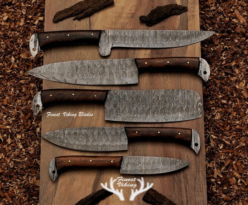 May include: An assortment of five Damascus steel knives with dark wooden handles and silver accents. The blades have a unique patterned design. The text "Finest Viking Blades" is visible on the wooden surface.