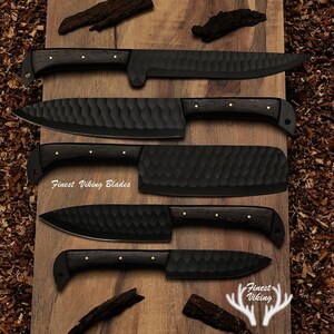 May include: Five black Viking blades with wooden handles and textured blades are displayed on a wooden surface. The text "Finest Viking Blades" is visible on the image. The knives vary in size and shape.