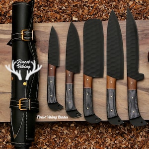 May include: A set of six black kitchen knives with wooden handles, arranged on a wooden surface. The knives are all different sizes and shapes, and they are all very sharp. The knives are labelled "Finest Viking Blades".