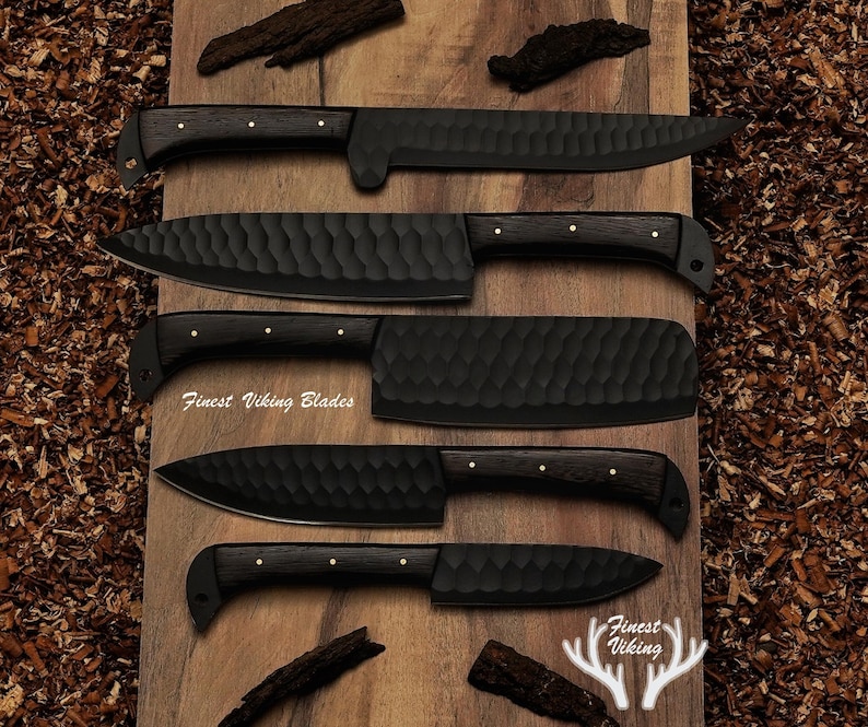 May include: Five black kitchen knives with wooden handles on a wooden surface. The knives have a textured, hammered finish. The text "Finest Viking Blades" is visible on one of the knives.