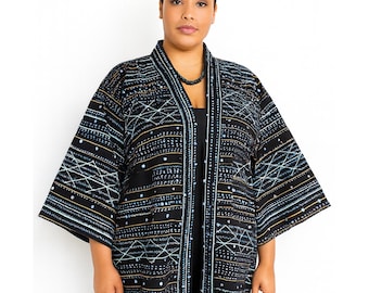 May include: A black kimono-style jacket with a geometric pattern in white, light blue, and gold. The jacket has wide sleeves and a collarless design. The pattern includes lines, dots, and diamond shapes. The jacket is worn over a black outfit.