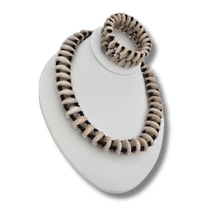May include: A white shell necklace and bracelet set with black string accents. The necklace is longer than the bracelet.