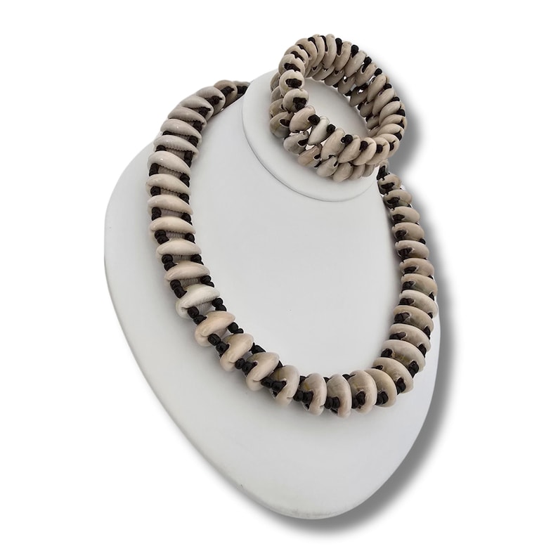 May include: A white shell necklace and bracelet set with black string accents. The necklace is longer than the bracelet.
