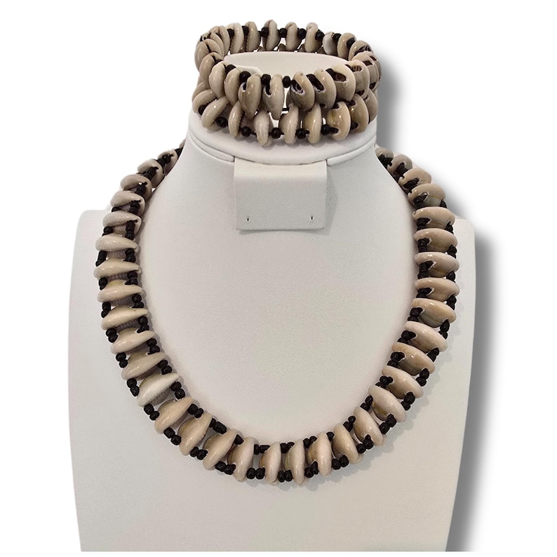 May include: A white shell necklace and bracelet set with black string accents. The necklace is longer than the bracelet.