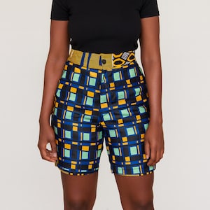 Könnte beinhalten: High-Waist-Shorts mit einem lebendigen geometrischen Muster. Die Shorts haben eine schwarze Basis mit einem Raster aus blauen, gelben und grünen Quadraten. Der Bund ist aus kontrastierendem gelb-schwarzem Stoff mit Knopfverschluss. Die Shorts sind knielang.