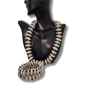 May include: A white and black shell necklace and bracelet set. The necklace is long and the bracelet is a single wrap. The necklace and bracelet are made of small, round shells.