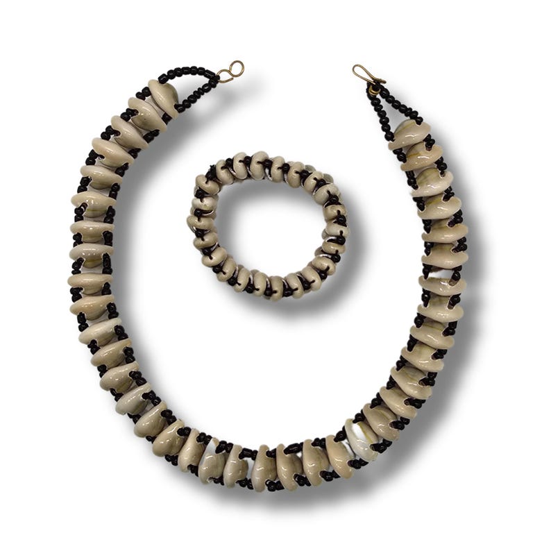 May include: A set of two necklaces made of beige shell beads and black string. The necklace is longer and the bracelet is shorter.