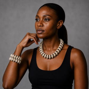 May include: A necklace and a matching double-strand bracelet set featuring smooth, off-white, ring-shaped beads separated by small, round, black spacer beads. The jewellery pieces are strung on a dark cord, creating a uniform, repeating pattern.