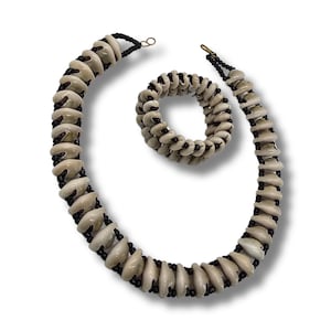 May include: A set of shell and black bead jewellery, including a necklace and a bracelet. The necklace and bracelet are made of white shell beads and black beads.