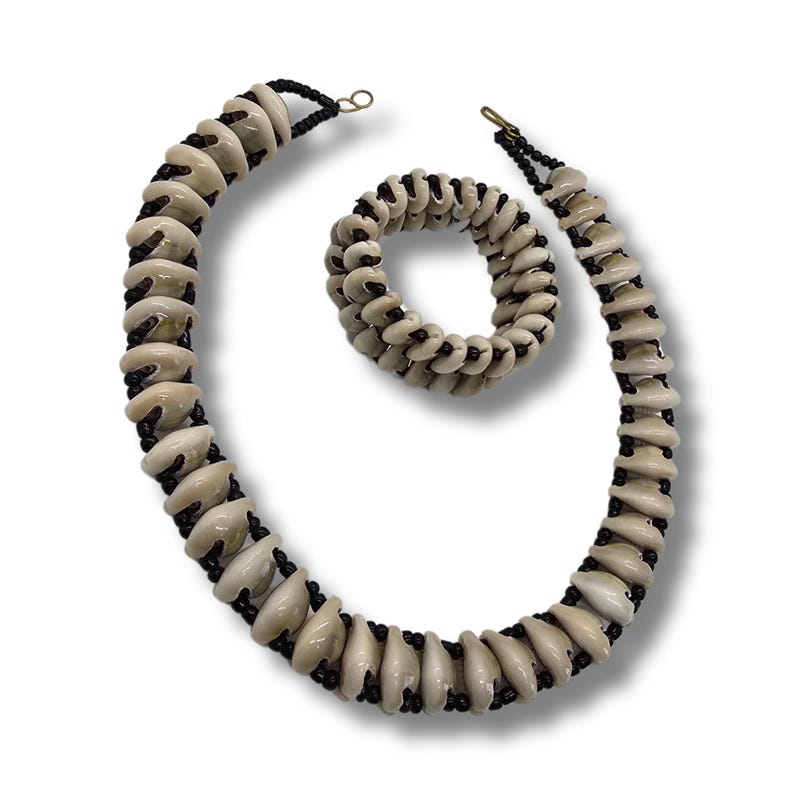 May include: A set of shell and black bead jewellery, including a necklace and a bracelet. The necklace and bracelet are made of white shell beads and black beads.