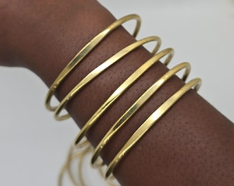 Puede incluir: Un conjunto de seis brazaletes finos de metal dorado pulido que se llevan juntos. Las pulseras presentan una superficie lisa y redondeada con un acabado reflectante, creando una apariencia apilada. Cada brazalete es un aro circular.