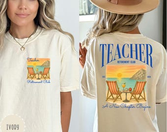 May include: Ivory-colored t-shirt with a graphic on the front and back. The front graphic shows beach chairs and drinks. The back graphic says "Teacher Retirement Club" with a beach scene and the text "A New Chapter Begins."
