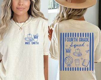 May include: An ivory t-shirt featuring blue graphics. The front displays a stack of books, an apple, a pencil cup, and the text "MRS. SMITH". The back features a large blue striped box containing the text "FOURTH GRADE Squad" with icons of a globe, books, a pencil cup, a paper airplane, and a notebook.
