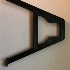 May include: Black plastic bracket with a rectangular opening in the center. The bracket is shaped like a V with the opening at the top.