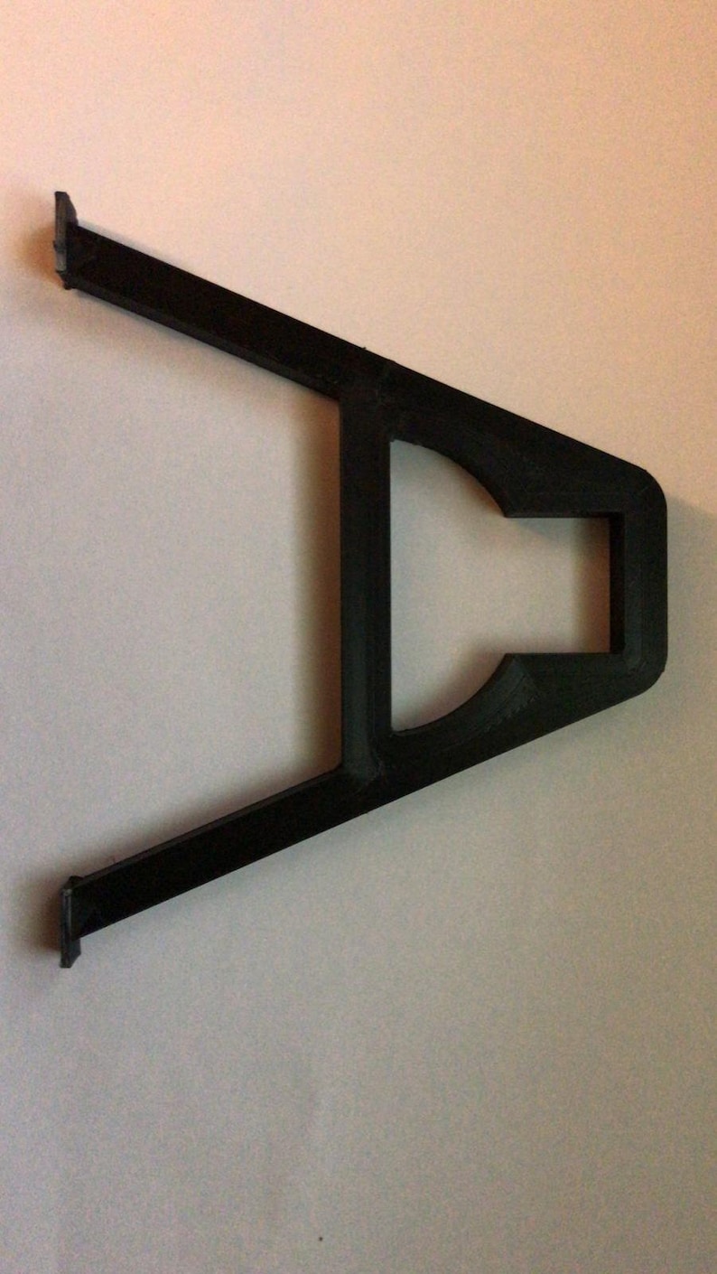 May include: Black plastic bracket with a rectangular opening in the center. The bracket is shaped like a V with the opening at the top.
