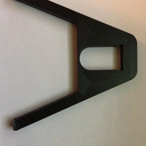 May include: A black plastic 3D printed object with a rectangular hole in the center and two arms extending out from the sides.
