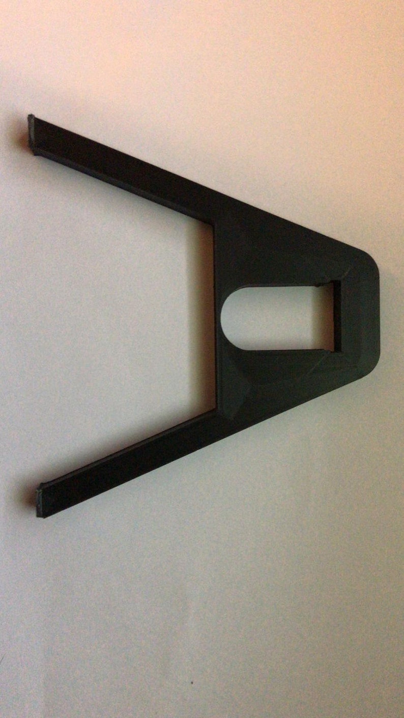 May include: A black plastic 3D printed object with a rectangular hole in the center and two arms extending out from the sides.