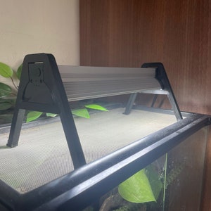 May include: Black metal stand with a light gray light fixture, mounted above a black mesh terrarium.