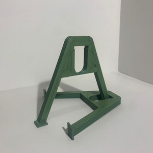 May include: A green plastic stand with a triangular base and a rectangular top. The stand is designed to hold a small object, such as a phone or a tablet.
