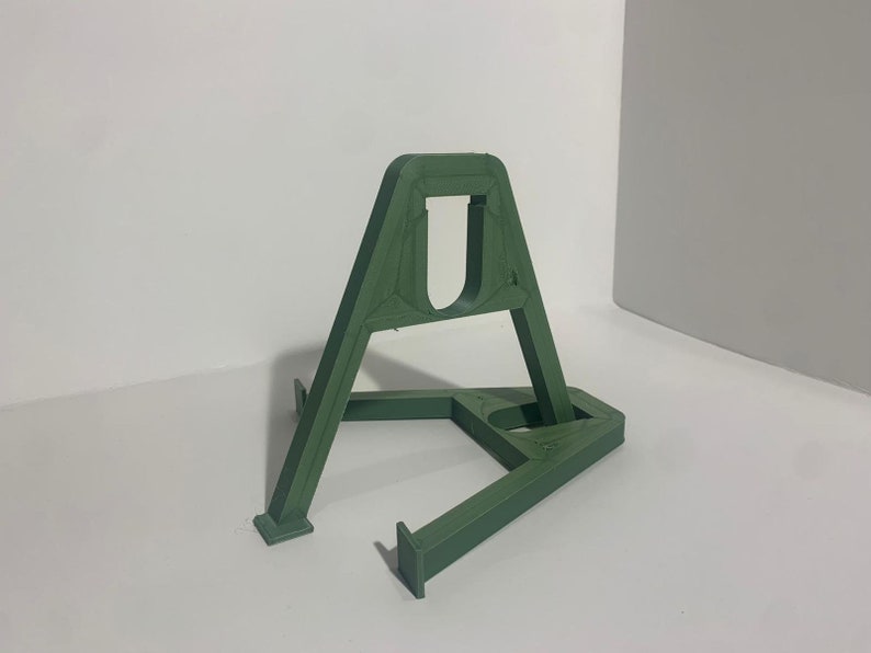 May include: A green plastic stand with a triangular base and a rectangular top. The stand is designed to hold a small object, such as a phone or a tablet.