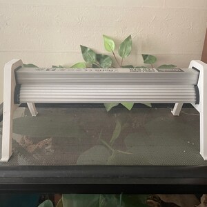 May include: White plastic stand with a white light fixture on top. The light fixture has a black trim and the text "Reptile UVB 10.0" printed on it.